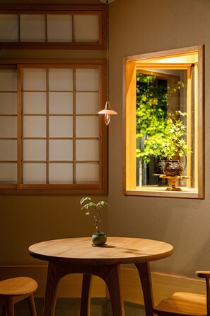 A room with a round wooden table, a hanging light fixture, and a window with a view of greenery. - Kyoran [6 min. by cab from Kyoto Stn.] Max. 6 people｜Renovation in 2025｜Private use of a machiya in a quiet alleyway｜Nishi Honganji temple nearby (京都市)