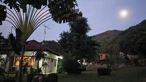 Un barrio residencial con casas, un árbol grande y una colina al fondo.