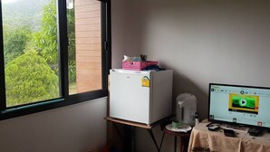 Una habitación con ventana, un refrigerador blanco, una mesa con una computadora y un enchufe de pared.