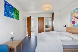 Une chambre à coucher moderne avec un grand lit, une tête de lit en bois, une table de chevet et un petit bureau.