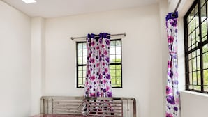 A room with a bed, a window with a curtain, and a view of greenery outside.