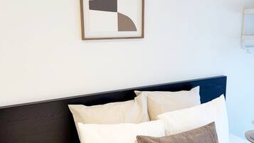 A bed with white bedding and a dark headboard, a framed abstract artwork on the wall, and a nightstand with a lamp.
