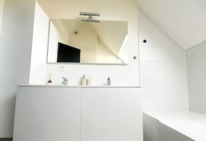 Un baño moderno con tocador blanco, un espejo grande y un solo grifo.