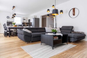 Un salon moderne avec un canapé d’angle, une table basse et des luminaires suspendus.