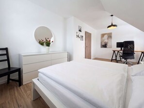 Une chambre à coucher avec un lit, un bureau, une chaise, un miroir et un mur décoré de tableaux.