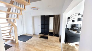 Ein modernes Interieur mit einer Holztreppe, einer gepolsterten schwarzen Bank, einem grauen Sofa und einer schwarzen Lampe.