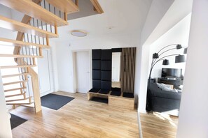 Un intérieur moderne avec un escalier en bois, un banc noir rembourré, un canapé gris et une lampe noire.