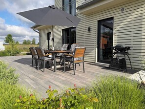 Une terrasse extérieure avec une table et des chaises, un barbecue et un grand parasol.