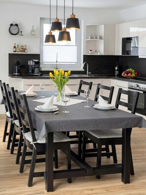 Une cuisine moderne avec un coin repas, comprenant une grande table dressée pour six personnes, des chaises noires et un éclairage suspendu.