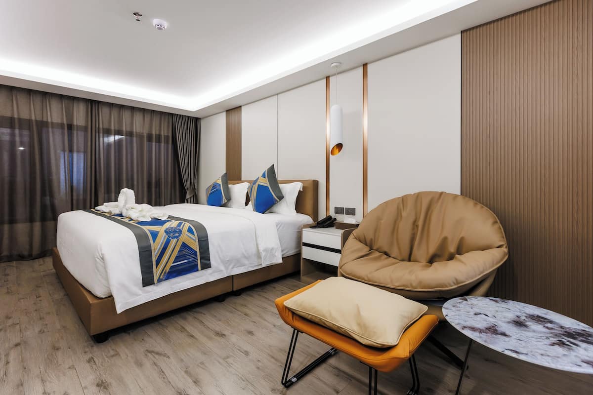 A hotel room with a large bed, a chair, a small table, and a nightstand.