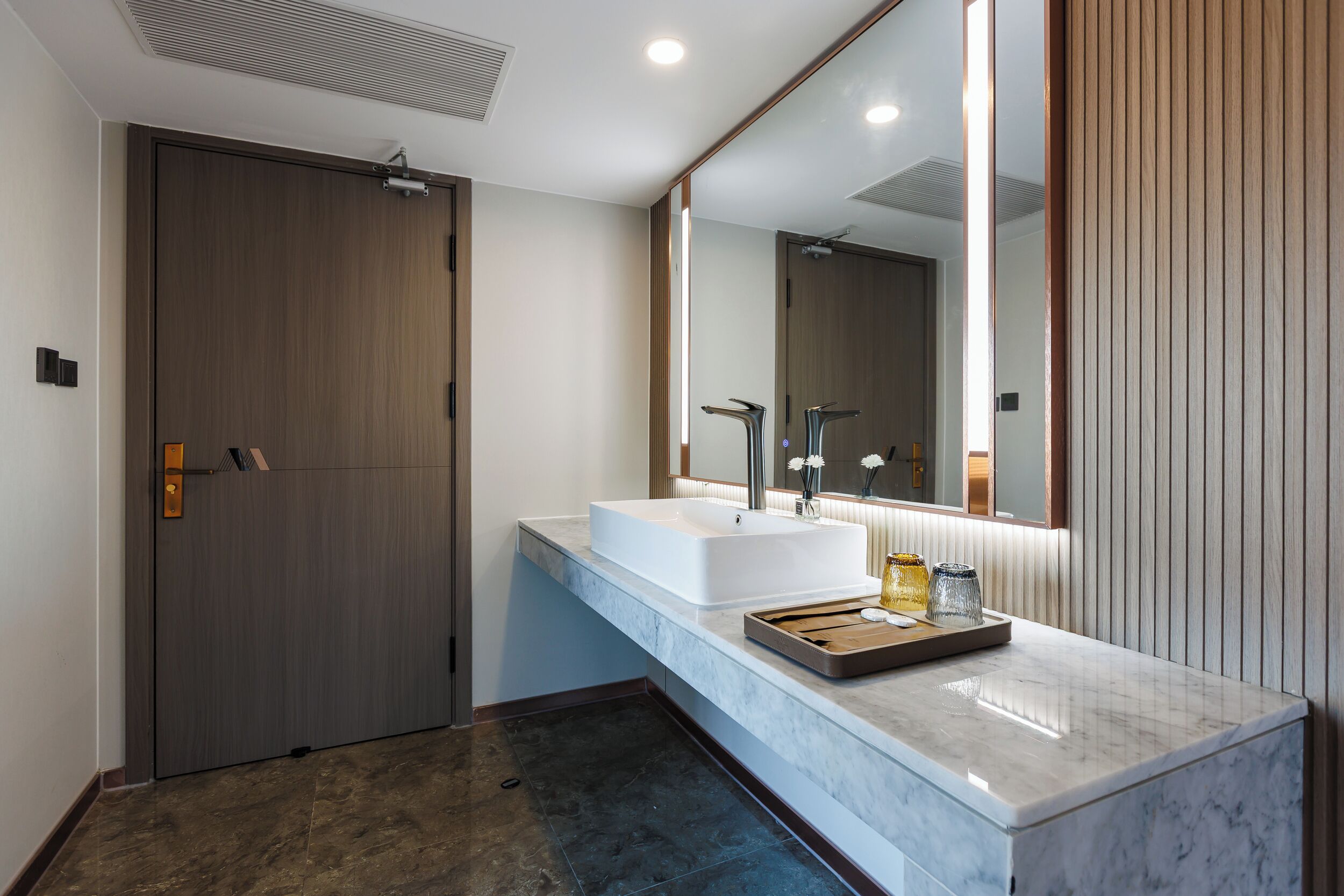 A modern bathroom with a large mirror, two sinks, and a wooden door.