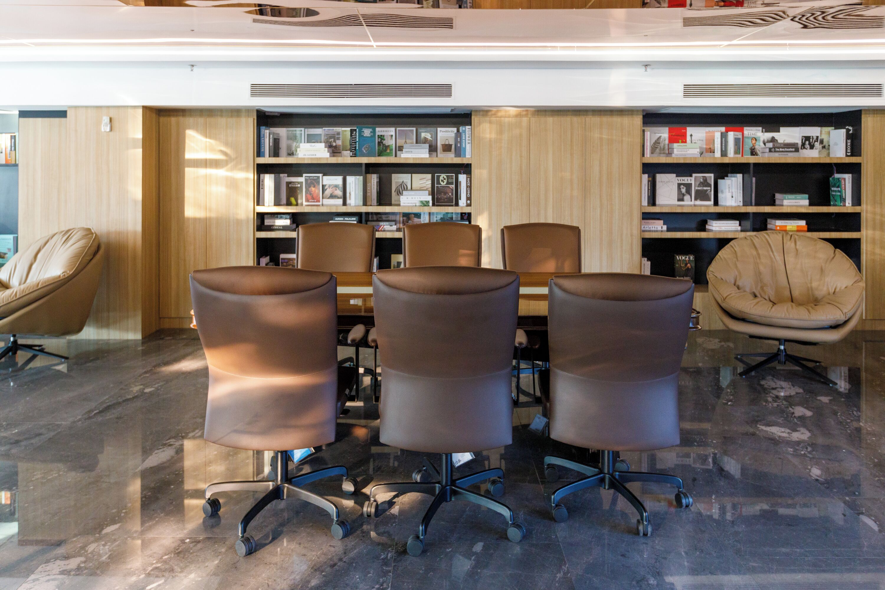A modern library with a marble floor, leather chairs, and bookshelves.