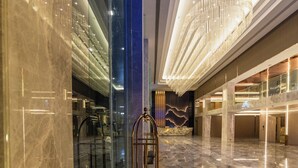 A spacious lobby with a central elevator, glass walls, and a modern chandelier. - MARQUIS HOTEL (Bangkok)