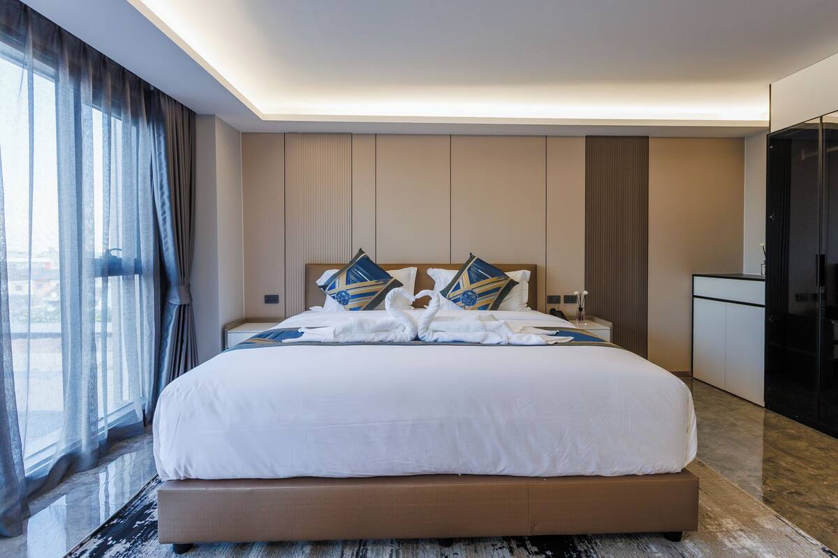 A modern hotel room with a large bed, a desk, and a view through the window.