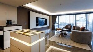 A modern living room with a flat-screen TV, a sofa, a coffee table, and a kitchen area with a built-in island. - MARQUIS HOTEL (Bangkok)