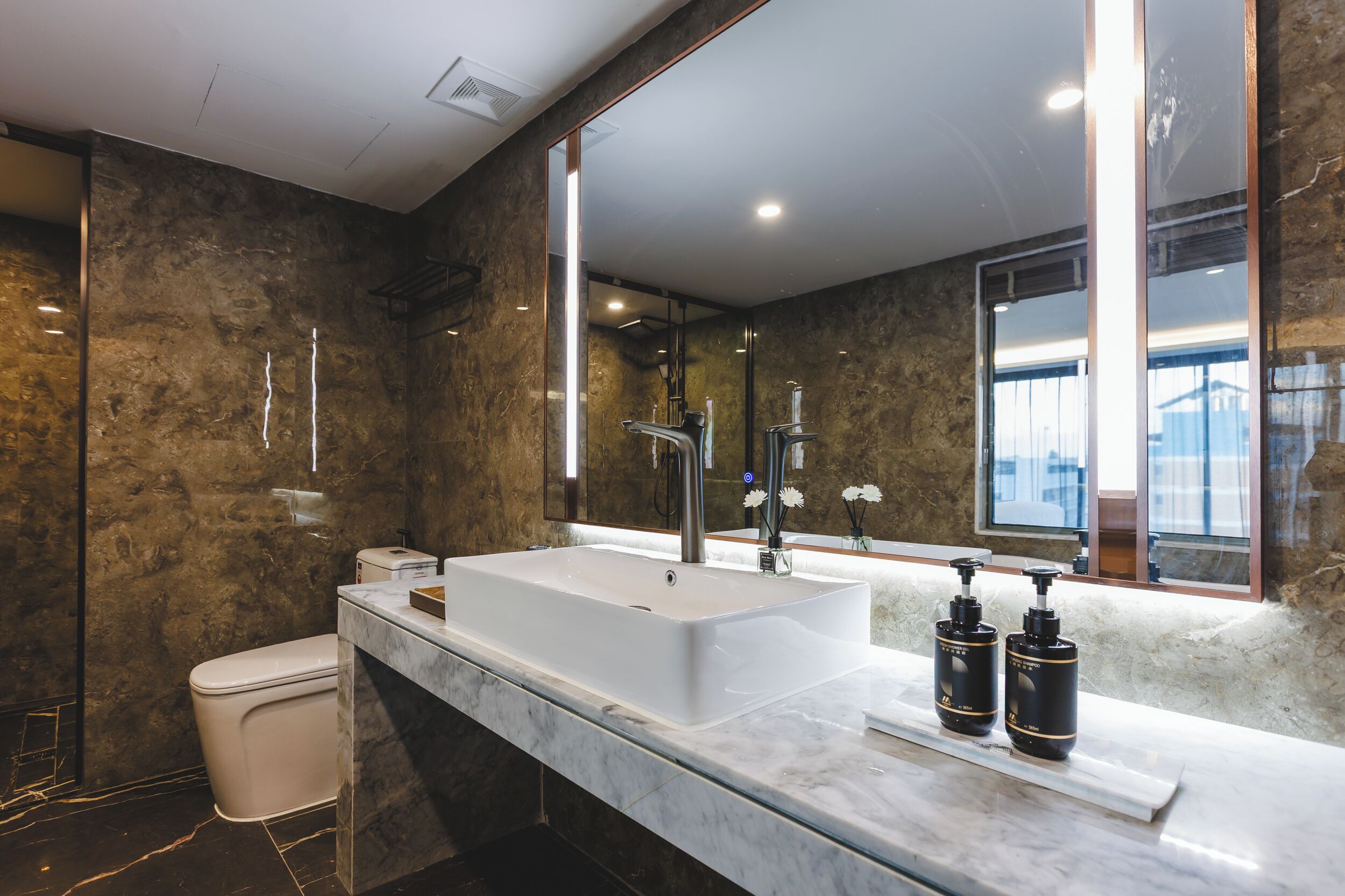 Un bagno moderno con un lavandino bianco ampio, uno specchio e due erogatori di sapone neri.