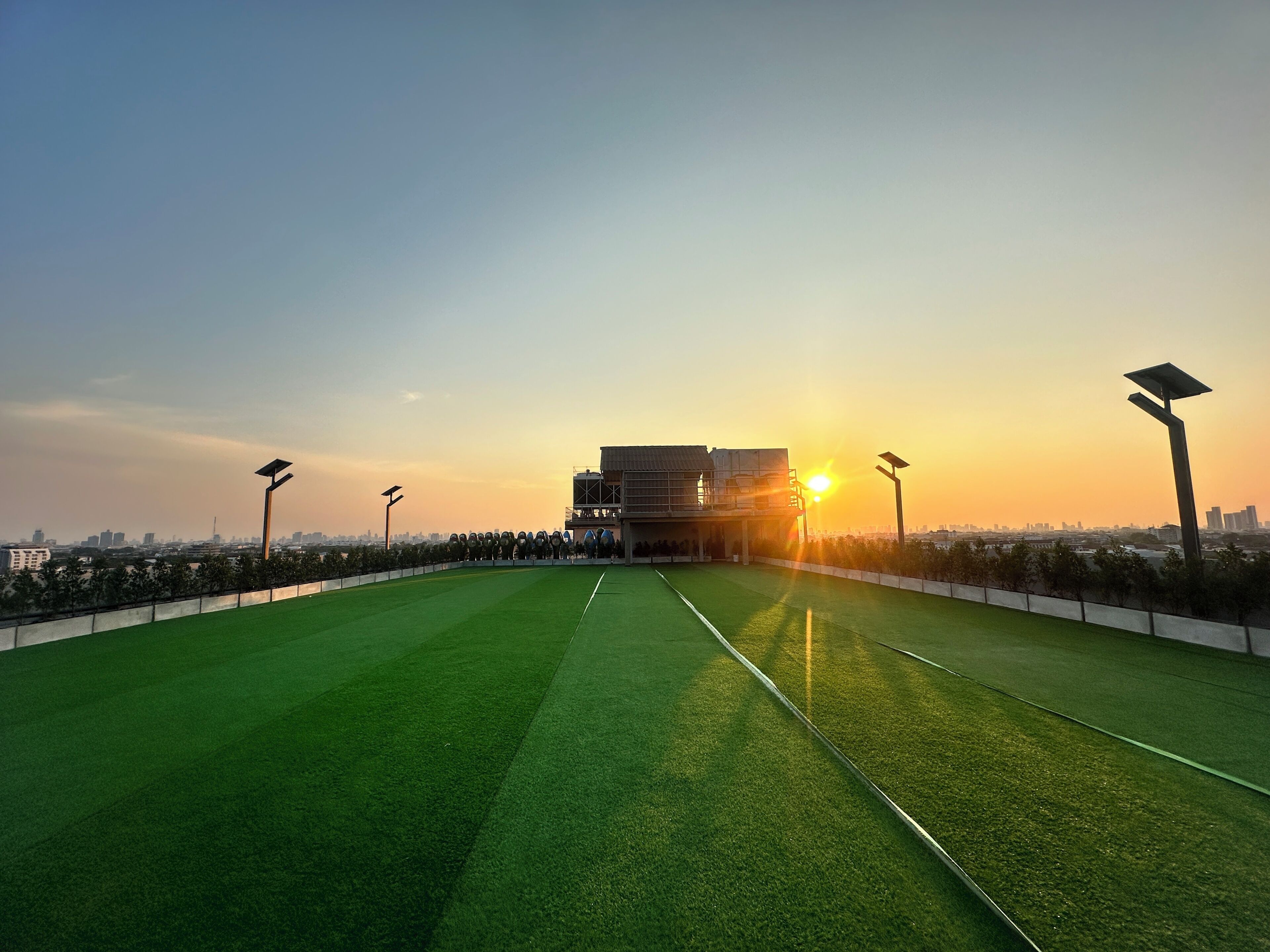 Un campo deportivo en la azotea con farolas solares, un cielo despejado y el perfil distante de una ciudad.