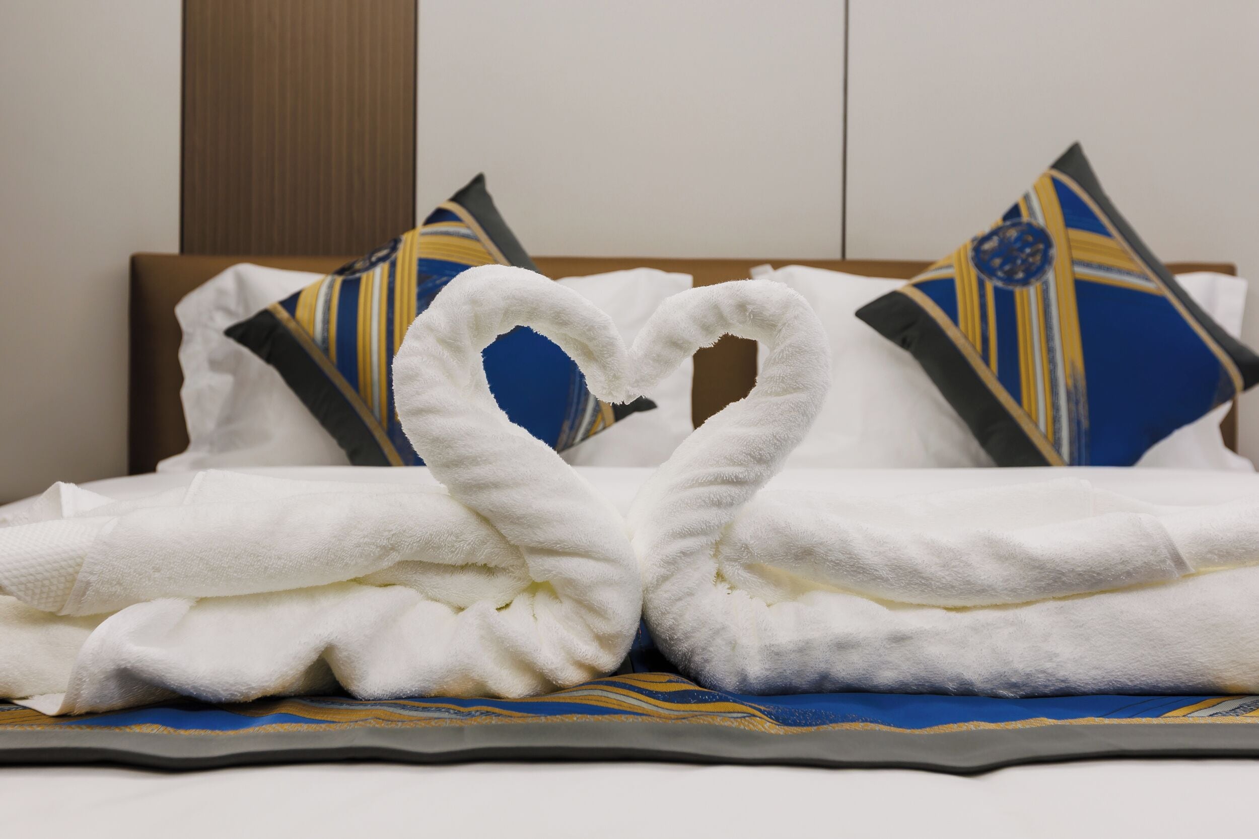 A bed with a heart-shaped towel arrangement and patterned pillows.