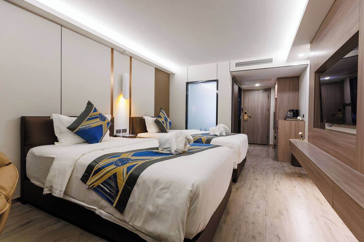 A hotel room with two beds, a TV, a desk, and a bathroom visible in the background.