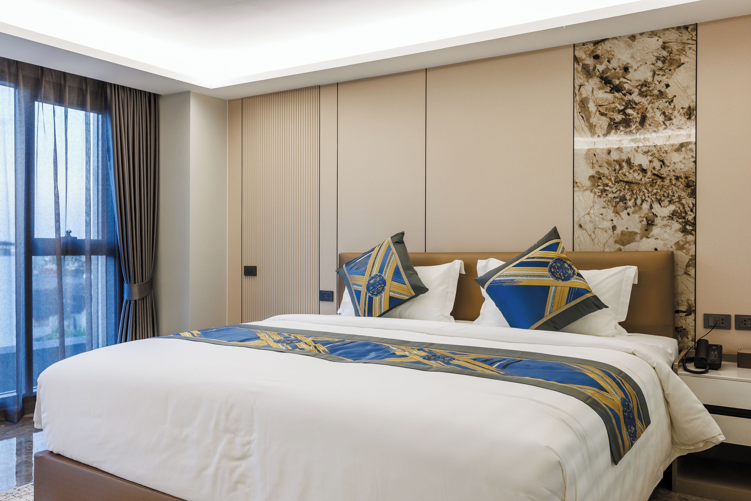 A hotel room with a large bed, a nightstand, a telephone, and a view of the outdoors.