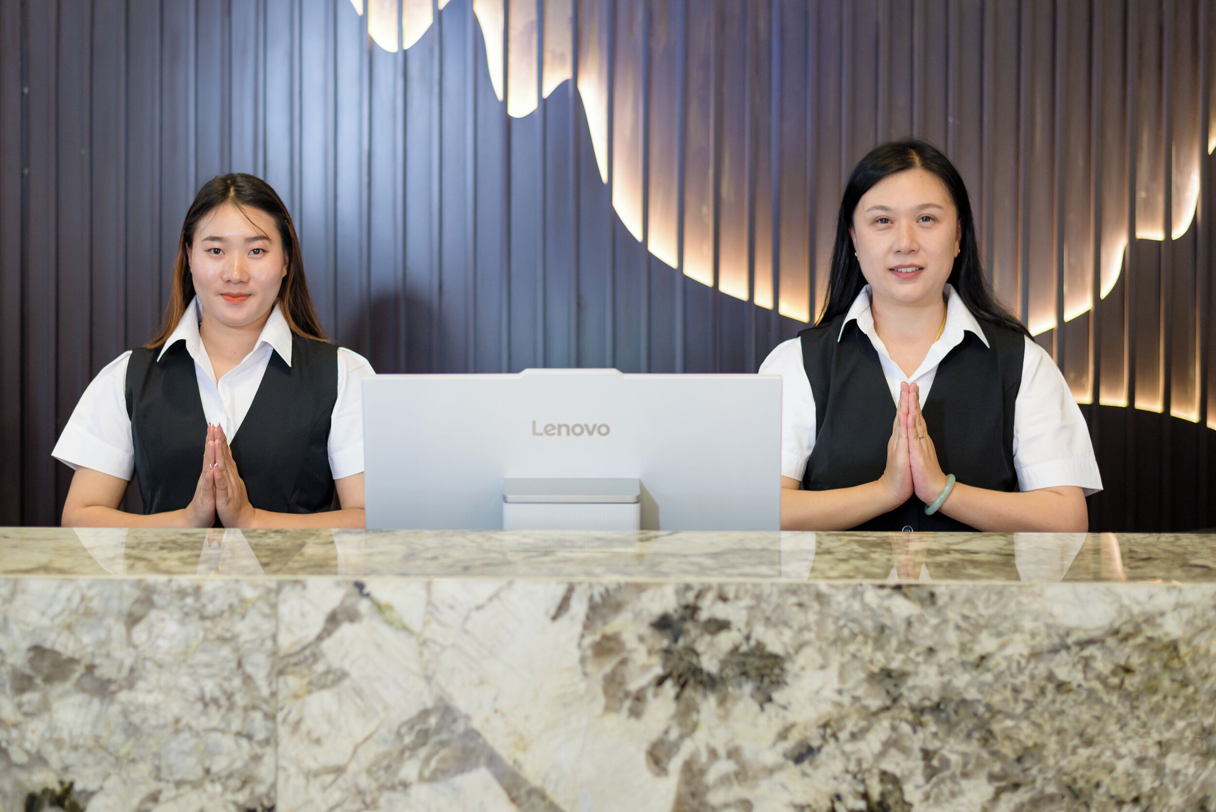 Due receptionist dietro una scrivania Lenovo con un piano di lavoro in marmo.