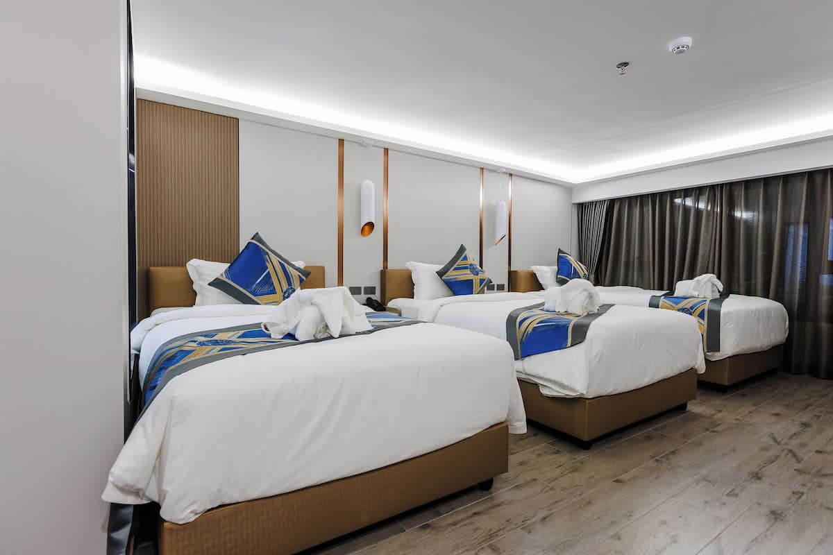 A hotel room with three beds, wooden flooring, and a modern design.