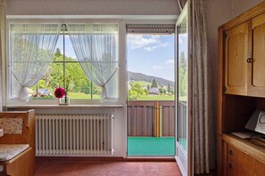 Une pièce donnant sur une pelouse verdoyante et des arbres, avec une chaise en bois, un radiateur et un meuble en bois.