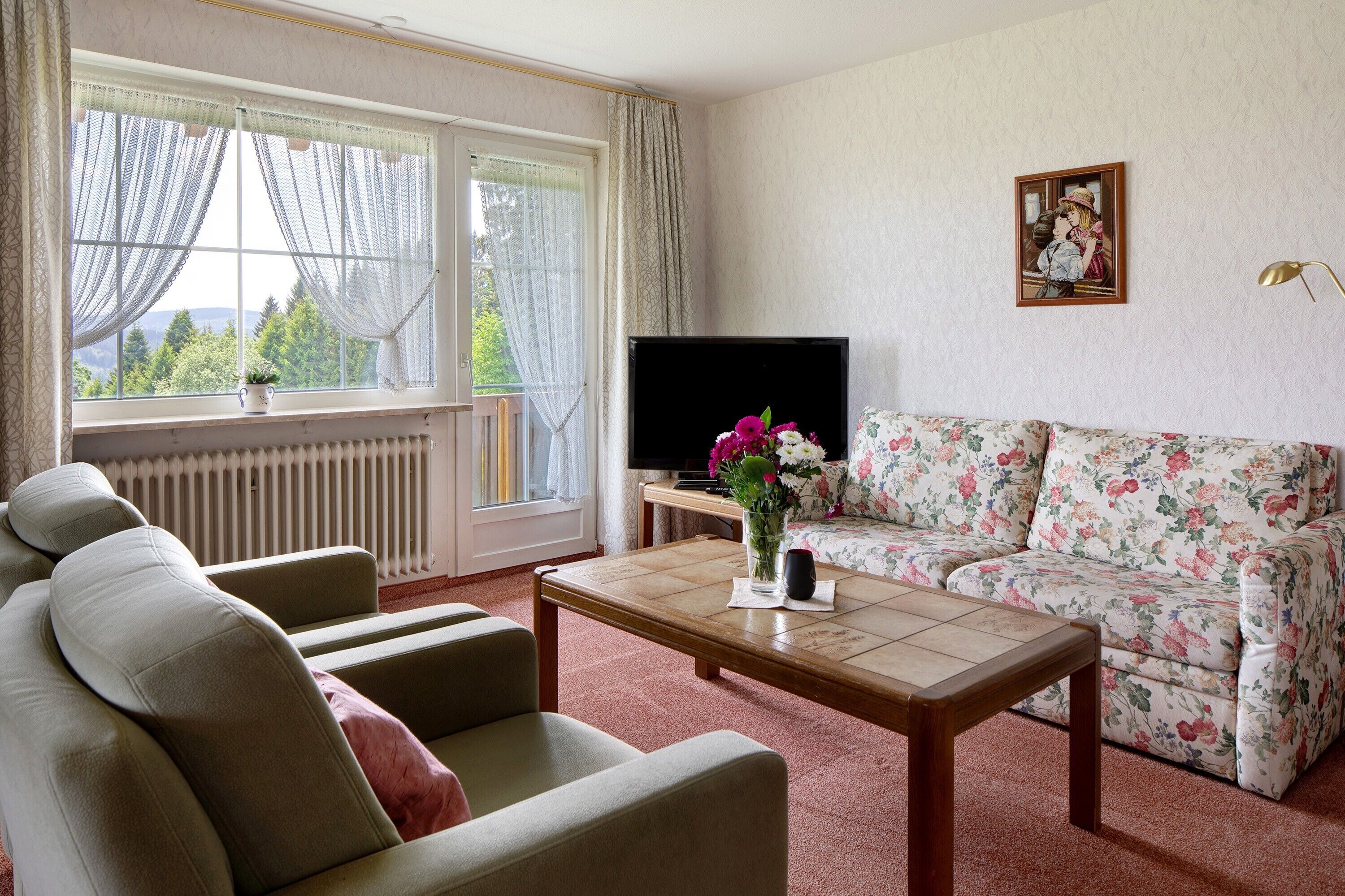 Ein Wohnzimmer mit einer Couch, Sesseln, einem Couchtisch, einem Fernseher und einem Fenster mit Vorhängen.