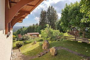 Une maison avec une véranda en bois, un chemin de pierres et un jardin agrémenté de rochers et d’arbres.
