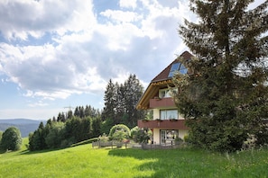 Ein zweistöckiges Haus mit geneigtem Dach, einem Balkon und Blick auf ein bewaldetes Gebiet.