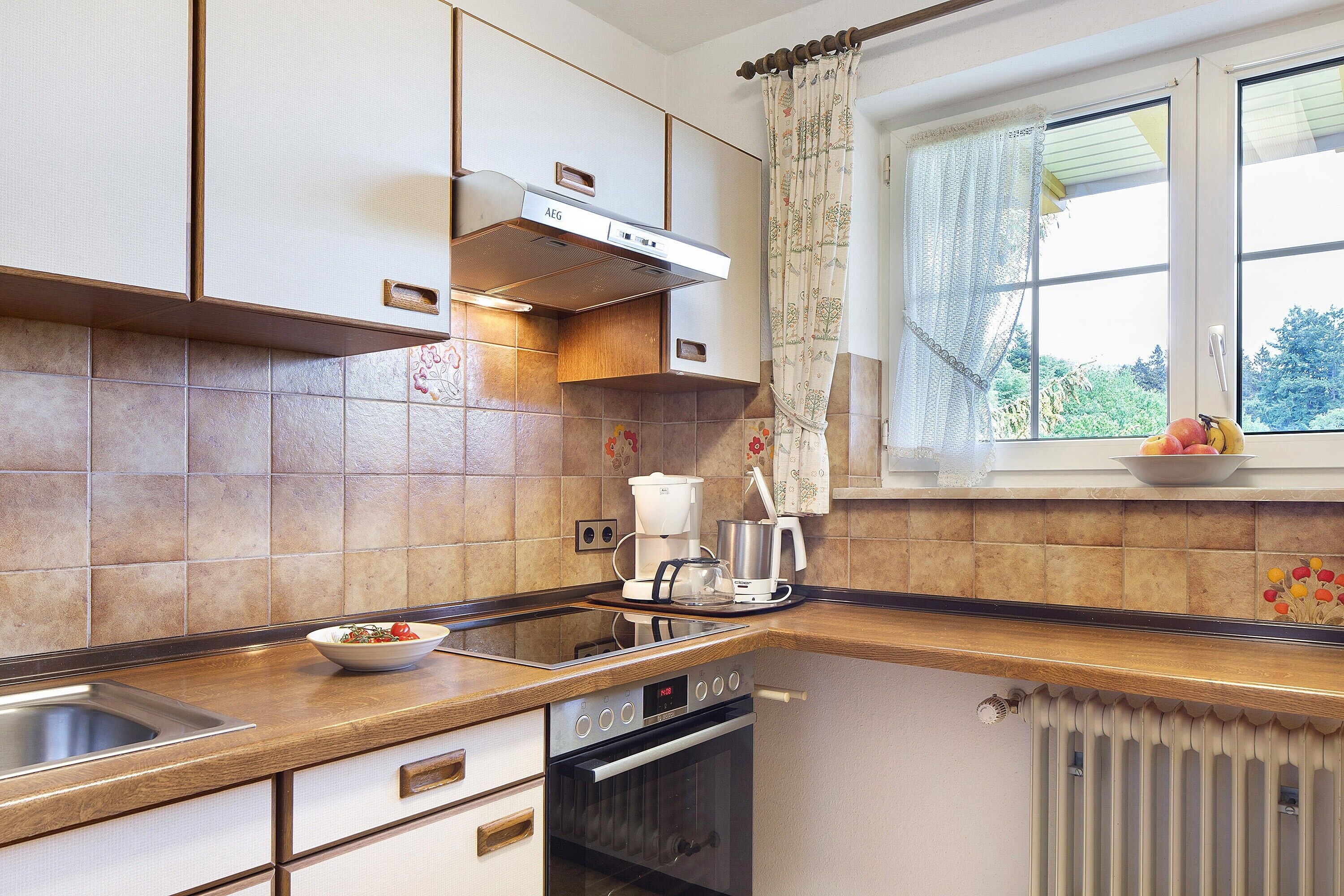 A modern kitchen with a built-in oven, a coffee maker, and a window with a view of trees.