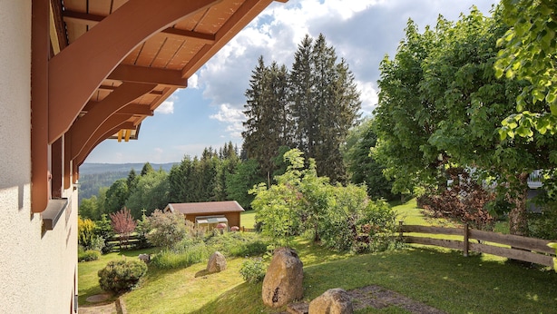 Ein Garten mit einer Holzdiele, einem Kiesweg und Blick auf ein bewaldetes Gebiet.