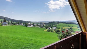Blick vom Balkon auf ein grünes Feld mit Häusern in der Ferne.