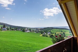 Blick vom Balkon auf ein grünes Feld mit Häusern in der Ferne.