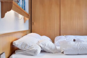 Ein ordentlich bezogenes Bett mit weißen Leinen und Kissen, ein Holz-Kopfteil und ein Regal mit Büchern und einer Lampe.