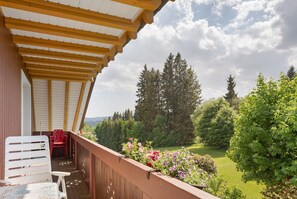 Ein Balkon mit einer Holz-Pergola, einem roten Stuhl und einem Tisch mit blumigem Tischlauf.