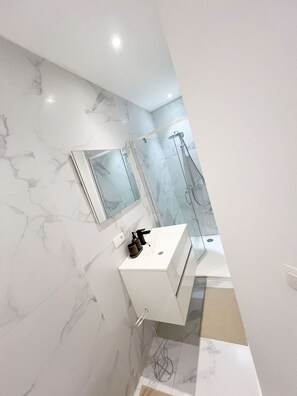 A modern bathroom with a marble wall, a white sink, a mirror, and a shower area. - Central 1BR With 1LR Apt Great Location (Ghent)