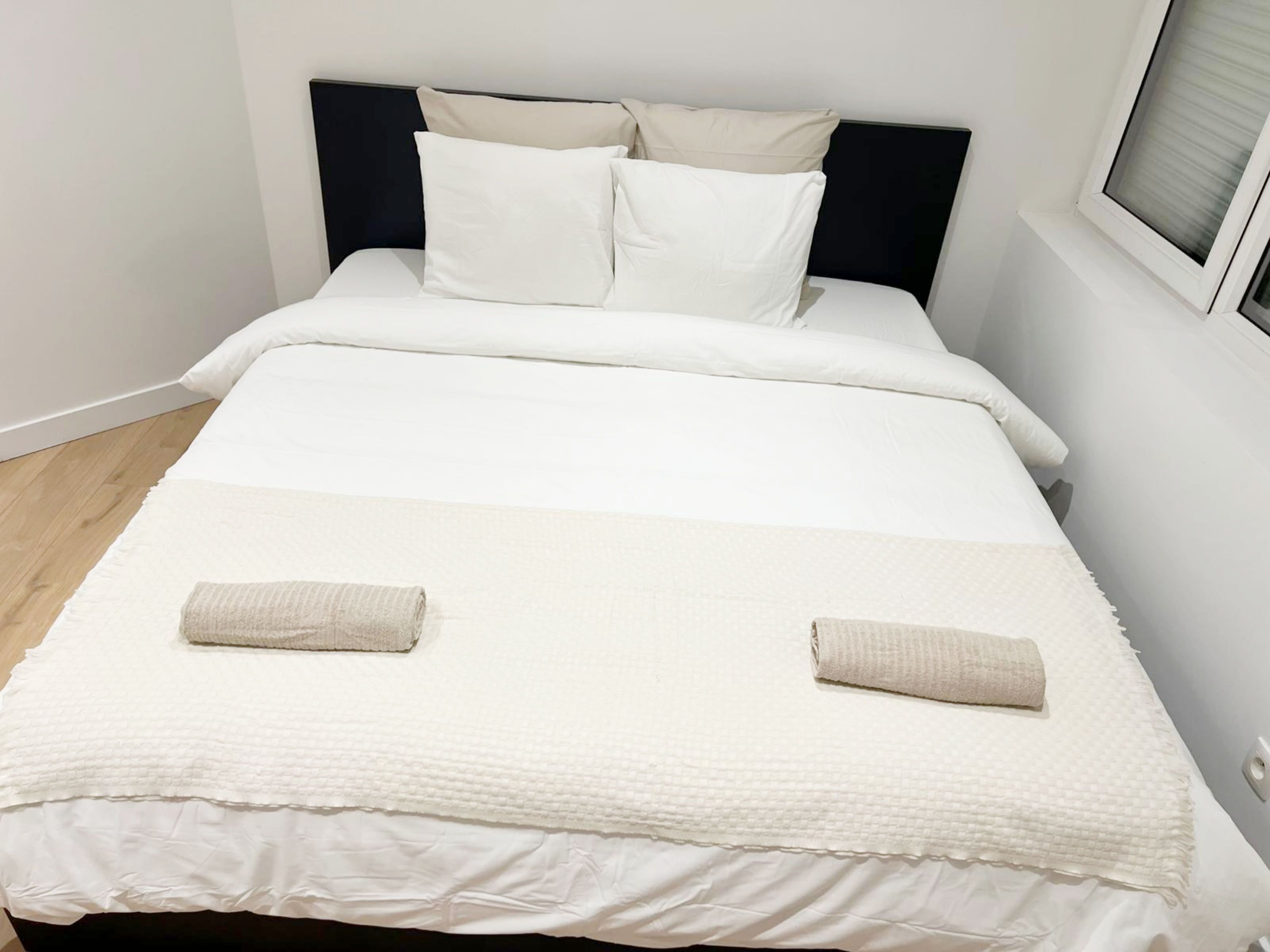 A neatly made bed with a white duvet, two pillows, and two folded towels.