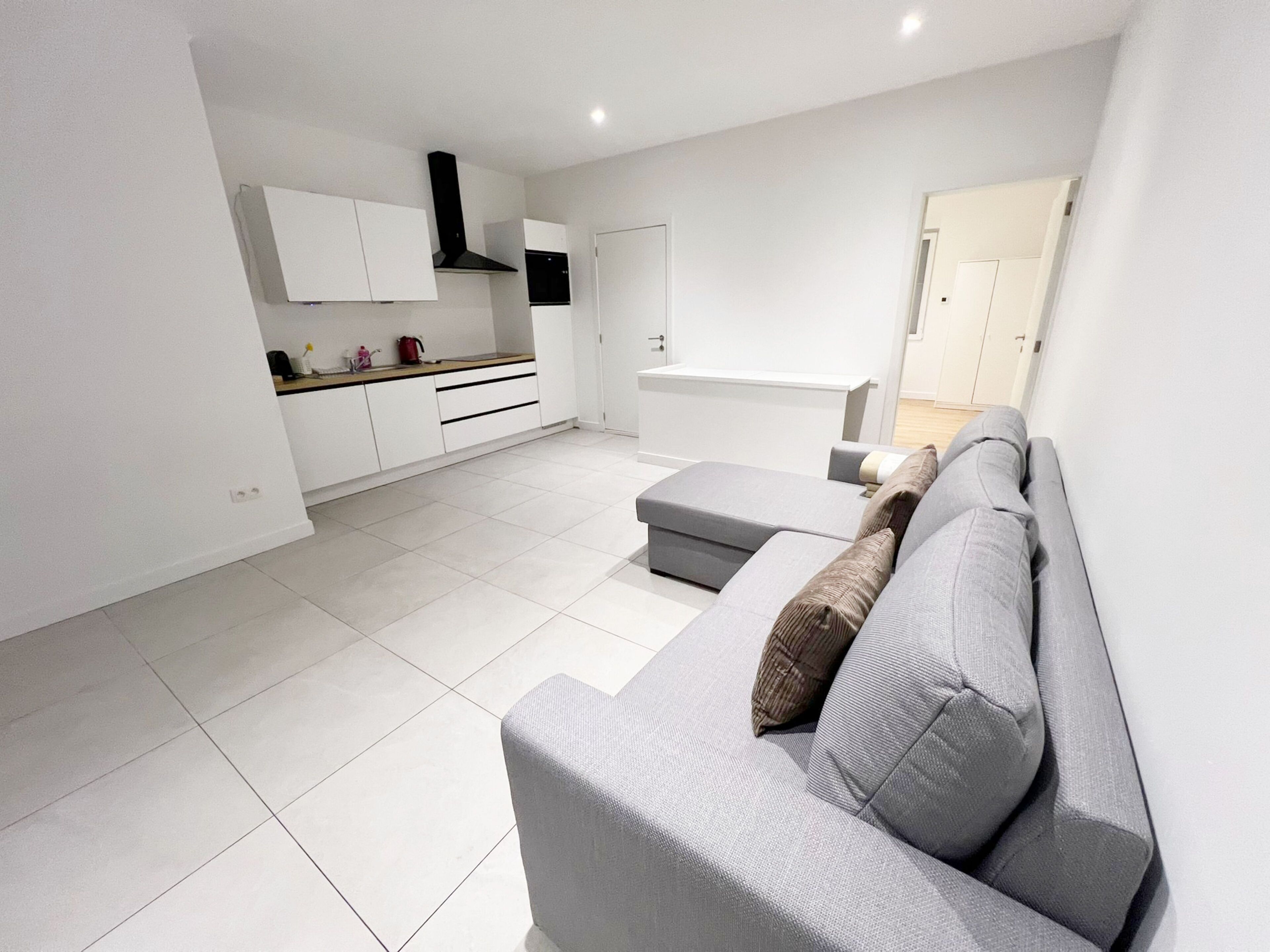 A modern kitchen with white cabinets and a grey sofa in a living area.