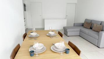 A dining area with a wooden table set for four, a grey sofa, and white walls.