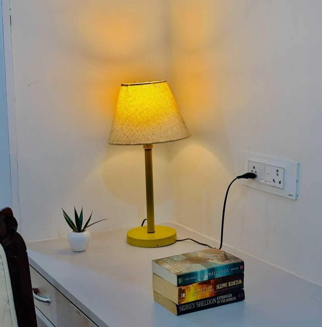 A bedside table with a lamp, a power outlet, and a stack of books.