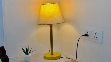 A bedside table with a lamp, a power outlet, and a stack of books.