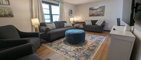 A living room with a sofa, ottoman, and a flat-screen TV.