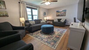 A living room with a sofa, ottoman, and a flat-screen TV.