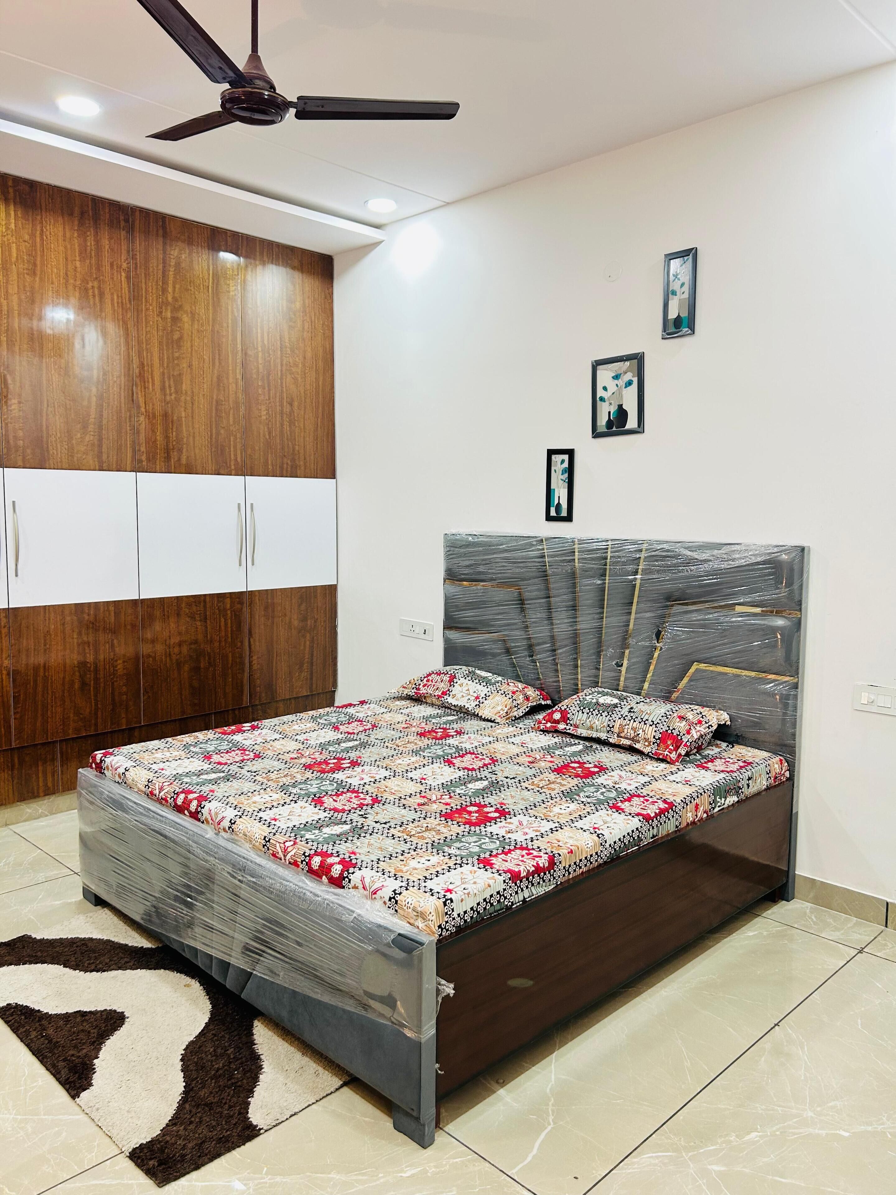 A bedroom with a bed, wardrobe, ceiling fan, and wall-mounted light fixture.