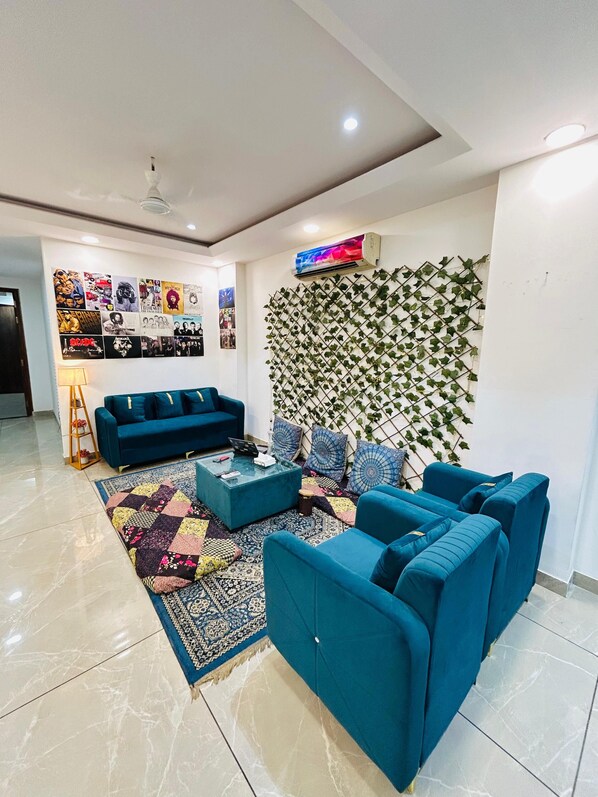 Un salon moderne avec un canapé bleu, un tapis à motifs et un mur décoré d’un motif végétal vert.