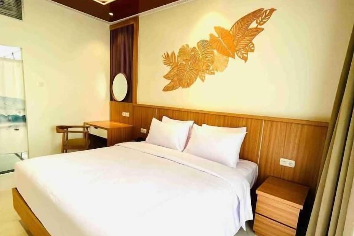 A modern hotel room with a large bed, wooden headboard, a wall-mounted artwork, a bedside table, and a nightstand.