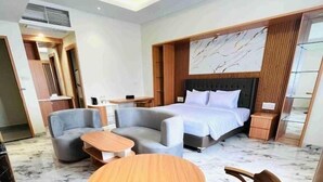 A modern hotel room with a bed, two sofas, a round wooden table, and two wooden chairs.