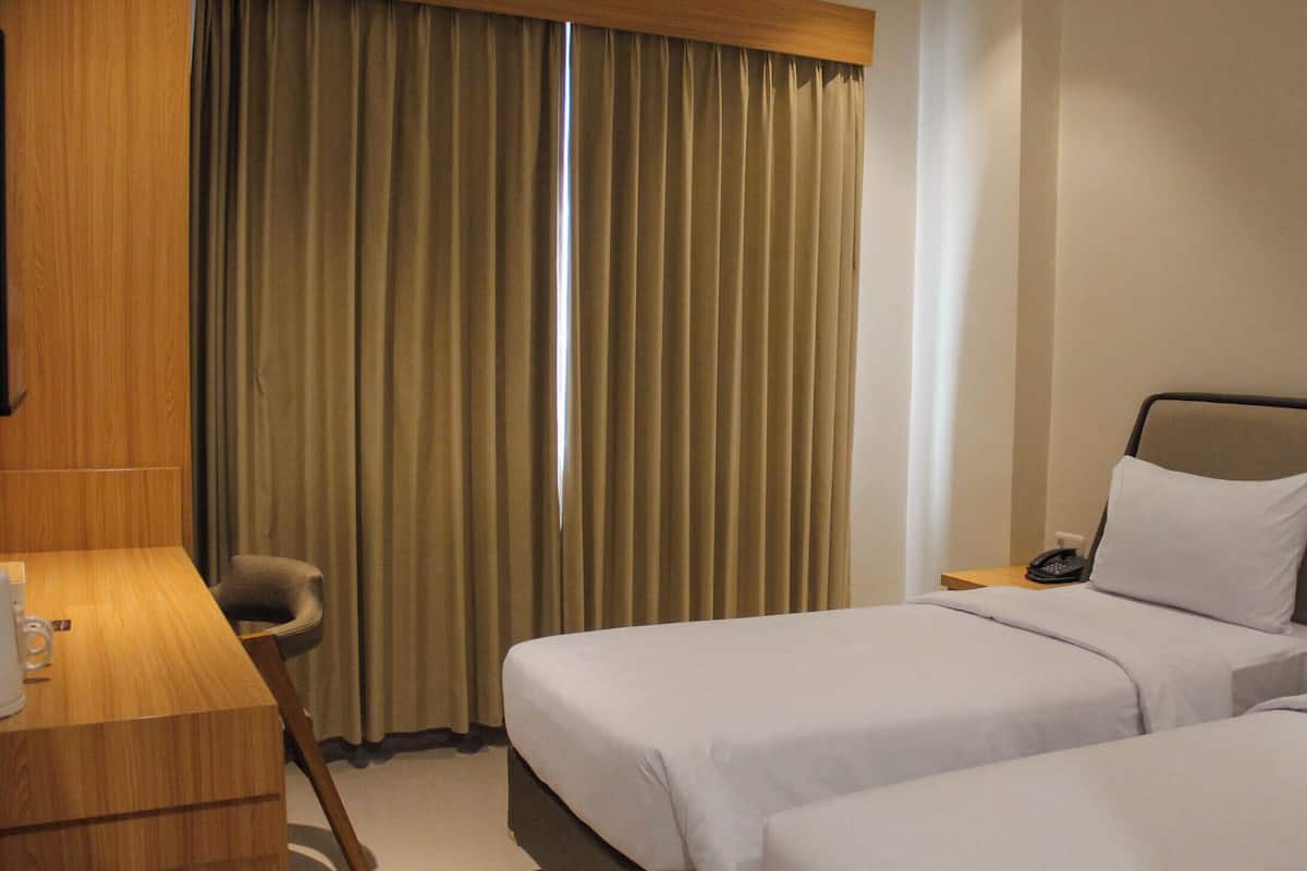 A hotel room with two beds, a desk, a chair, a telephone, and a window with curtains.