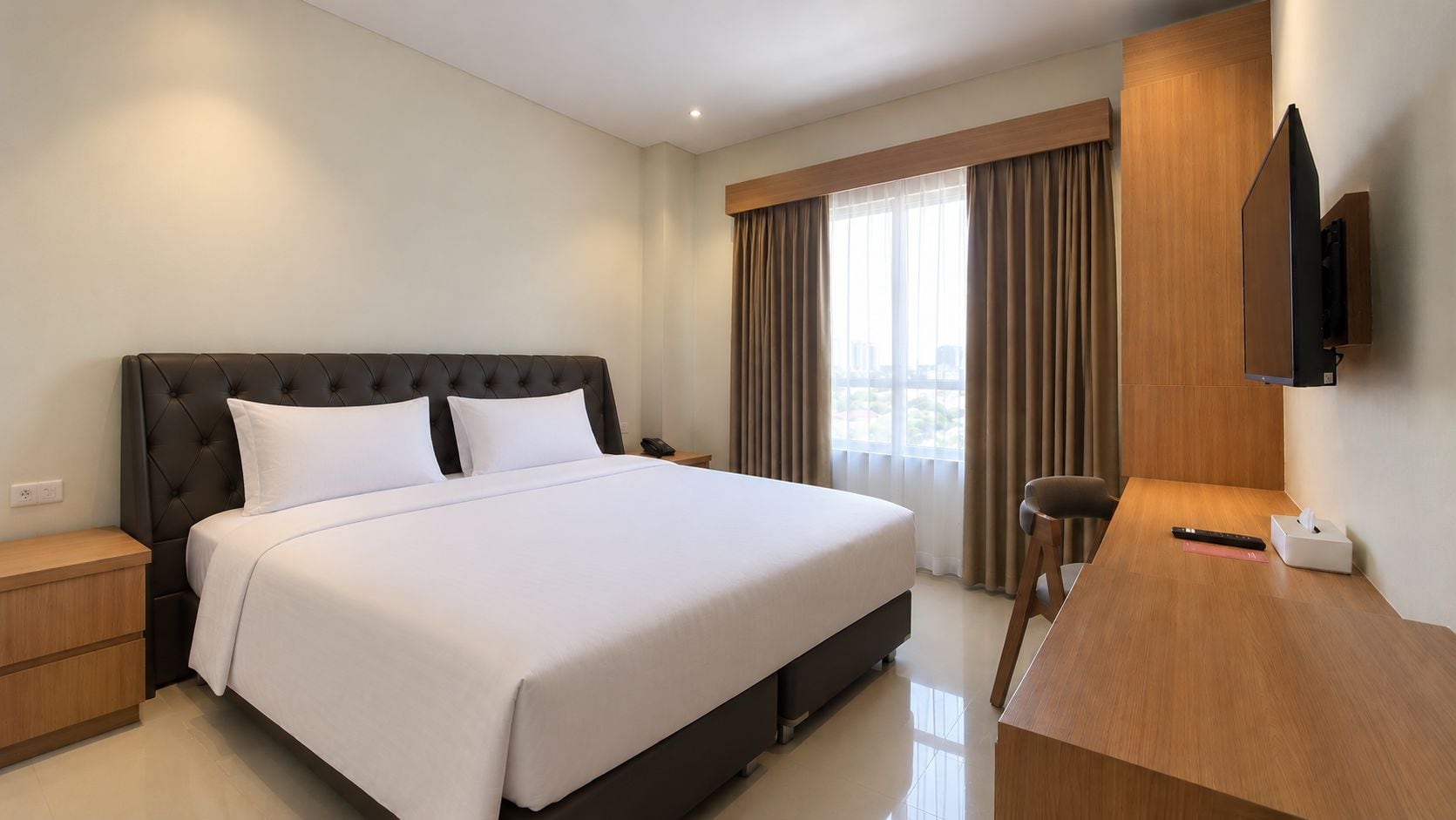 A hotel room with a large bed, a desk, a chair, a television, and a window with curtains.